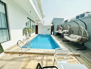 A modern outdoor pool area with a wooden deck, a pool, and wicker chairs. - Lekki Villas (Lekki)