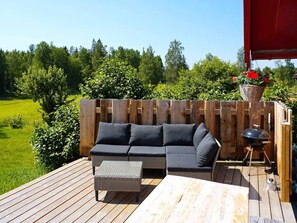Una terraza de madera con un sofá de mimbre, una mesita y una parrilla.