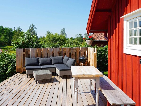 Una terraza de madera con un sofá y una mesa, rodeada por una valla de madera y un edificio rojo.