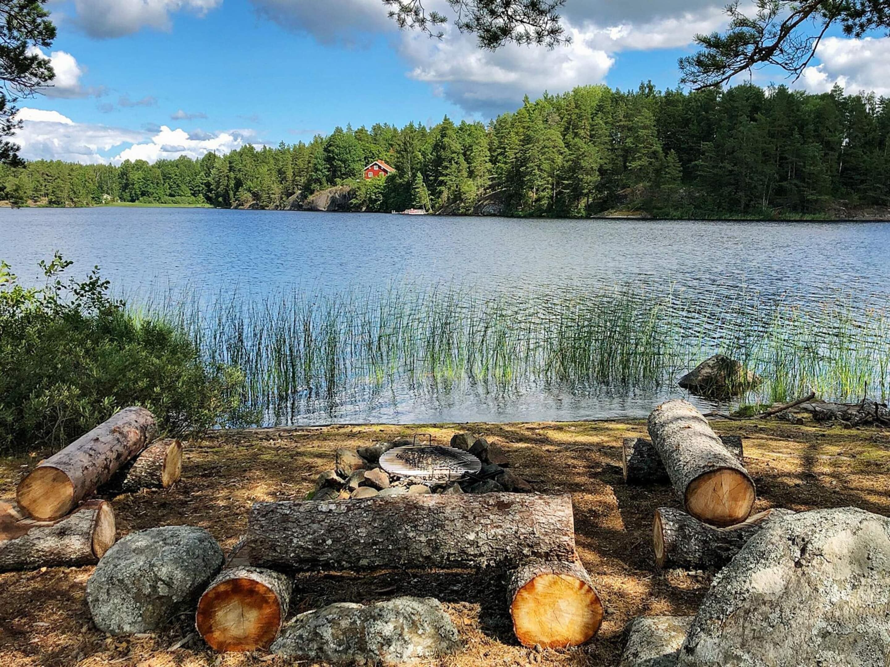A lakeside scene with a cabin, logs, and a fire pit.