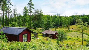 A red cabin with a metal roof, surrounded by lush greenery and trees. - 5 Person Holiday Home in Mellosa (Flen)