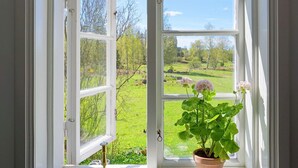 An open window with a view of a green landscape and a potted plant with flowers. - 5 Person Holiday Home in Mellosa (Flen)