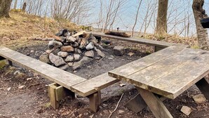 A wooden picnic table with benches, a fire pit with rocks, and a view of a lake. - 4 Person Holiday Home in Granna (Gränna)