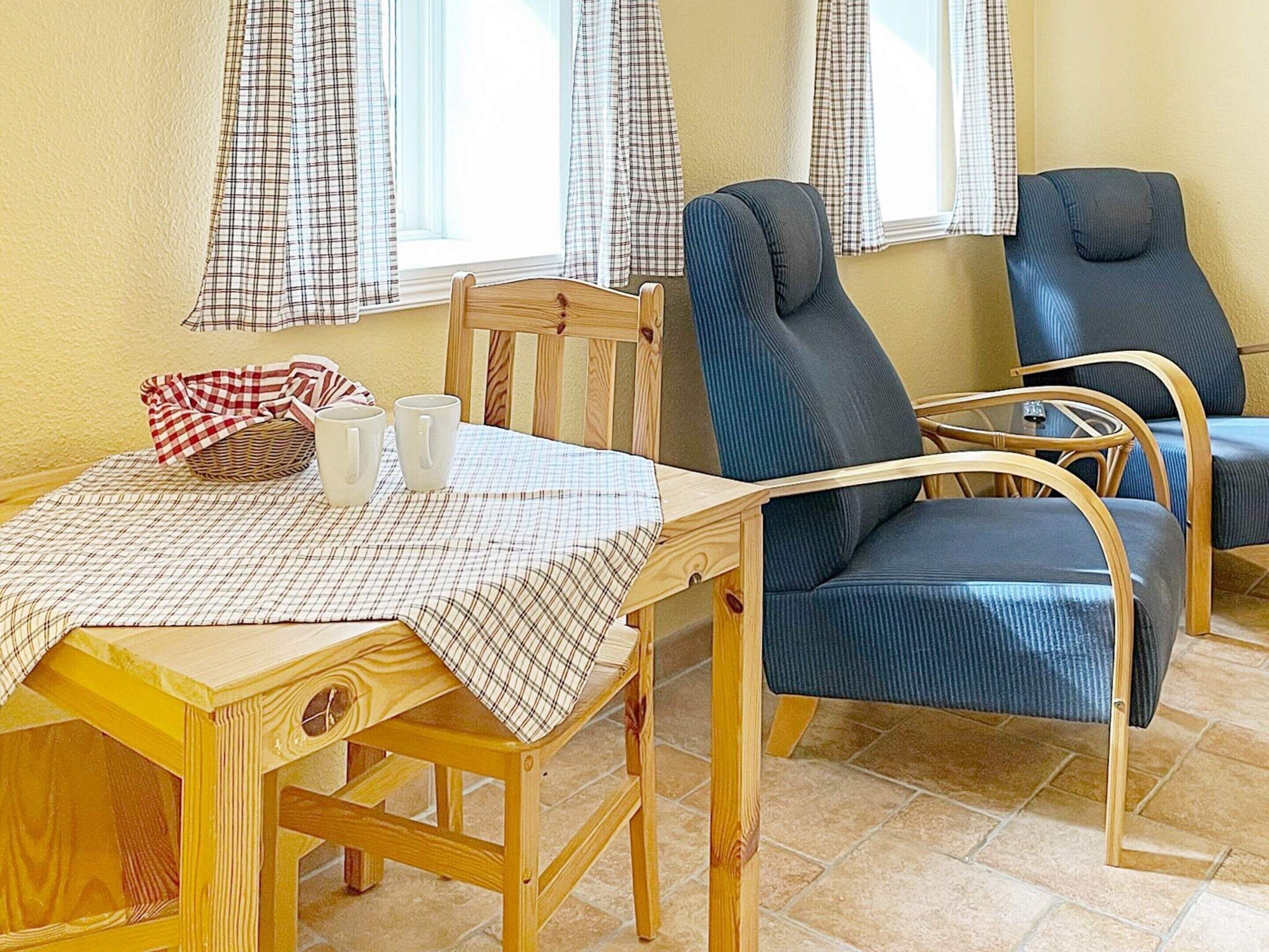 A wooden dining table with a checkered tablecloth, two blue chairs, and a wicker basket with a red and white checkered cloth.