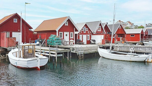 A waterfront with red buildings, docked boats, and a calm water surface. - 6 Person Holiday Home in Kungshamn (Kungshamn)