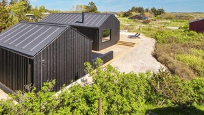 A modern, minimalist cabin with a sloped roof and a wooden deck. - 5 Star Holiday Home in Romo (Rømø)