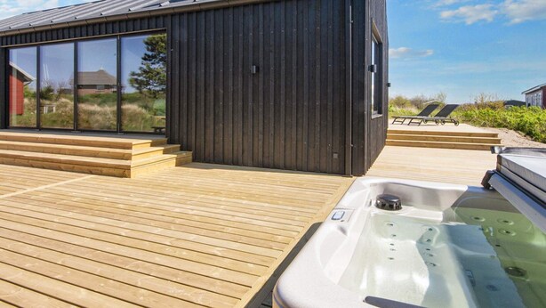 A modern building with a large glass window, a wooden deck, and a hot tub. - 5 Star Holiday Home in Romo (Rømø)