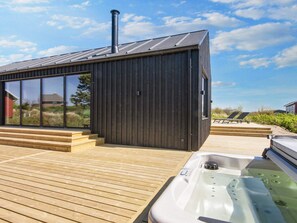 A modern building with a large glass window, a wooden deck, and a hot tub. - 5 Star Holiday Home in Romo (Rømø)