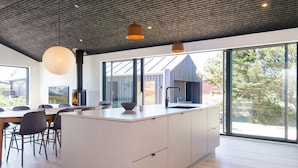 A modern kitchen with a large island, large windows, and a dining area with chairs. - 5 Star Holiday Home in Romo (Rømø)