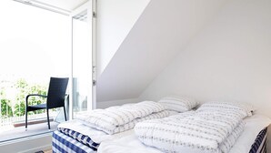 Une chambre à coucher avec un lit, deux oreillers, une chaise et une vue sur l’extérieur.