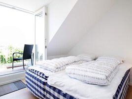 Un dormitorio con cama, dos almohadas, una silla y vistas al exterior.
