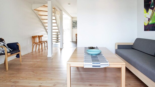Un salon moderne avec un plancher en bois, un canapé, une table basse sur laquelle se trouve un bol, un tapis à rayures et un escalier menant à une autre pièce.