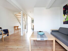 Una sala moderna con suelo de madera, un sofá, una mesa de centro con un cuenco, un tapete a rayas y una escalera que lleva a otra habitación.