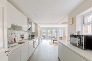 A modern kitchen with white cabinetry, a built-in oven, and a dining area with a table and chairs. - Contemporary 2BD Cottage-Style Flat, Hackney (Greater London)