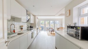 A modern kitchen with white cabinetry, a built-in oven, and a dining area with a table and chairs. - Contemporary 2BD Cottage-Style Flat, Hackney (Greater London)