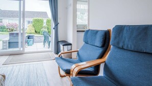 Uma sala de estar moderna com um sofá azul, uma mesa de centro de madeira e vista para um jardim através de uma porta de vidro deslizante.