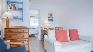 Uma sala de estar moderna com um sofá branco, uma poltrona azul, cômoda de madeira e estante de livros.