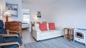 Uma sala de estar moderna com um sofá branco, poltronas azuis, um aparador de madeira e um pequeno aquecedor branco.