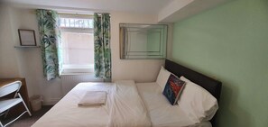 Hotelkamer met een bed, bureau, stoel, raam met gordijnen, radiator en spiegel aan de muur.