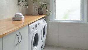 A modern laundry room with a washing machine, dryer, and a window providing natural light. - Sunny, spacious three bedroom apartment with views (Battery Point)