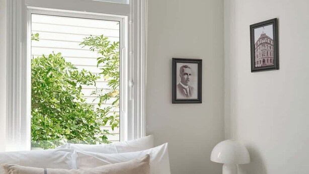 A bedroom with a bed, a window with blinds, a bedside table with a lamp, and two framed pictures on the wall. - Sunny, spacious three bedroom apartment with views (Battery Point)