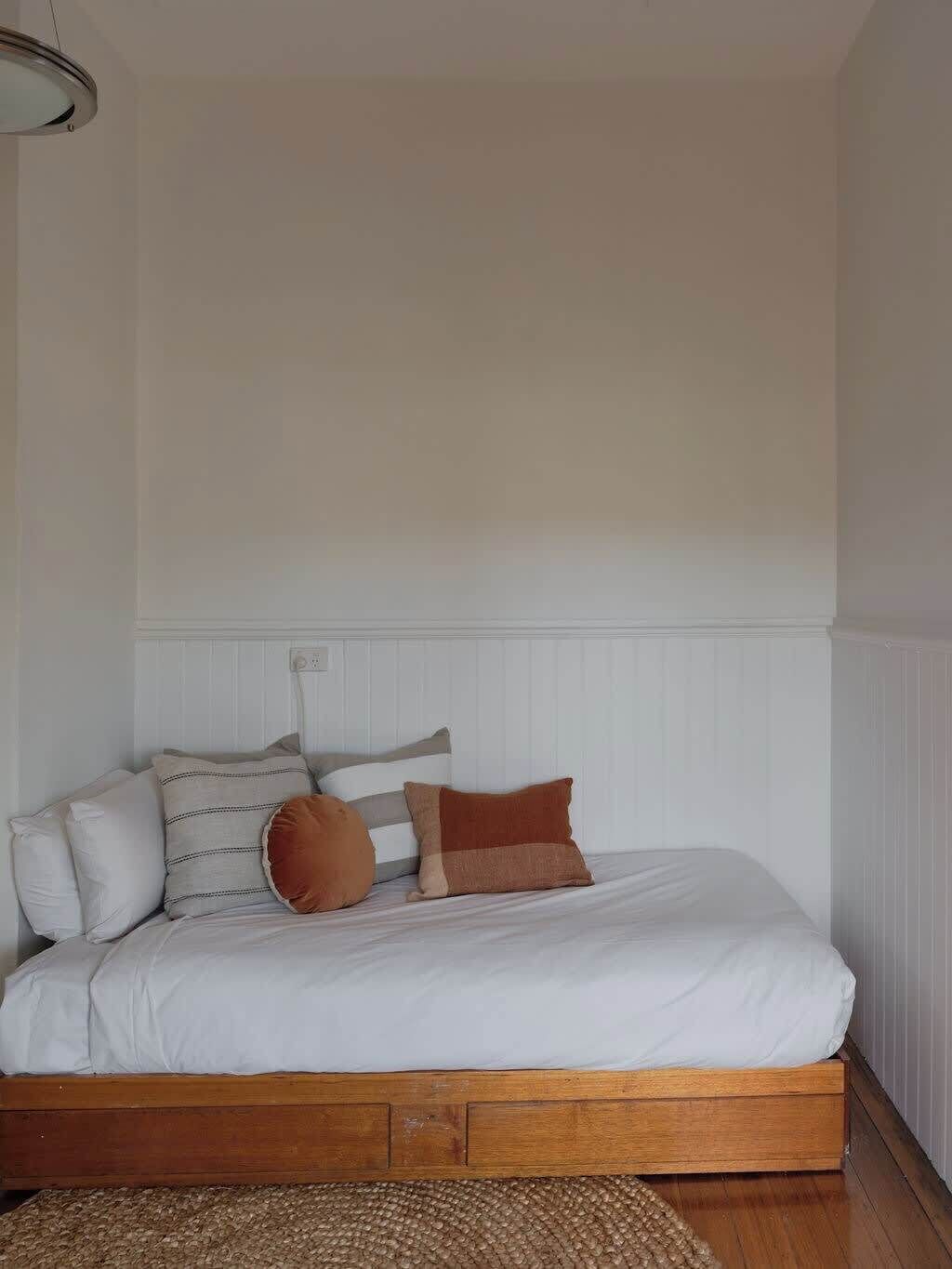 A bedroom with a wooden bed frame, white bedding, and several pillows.