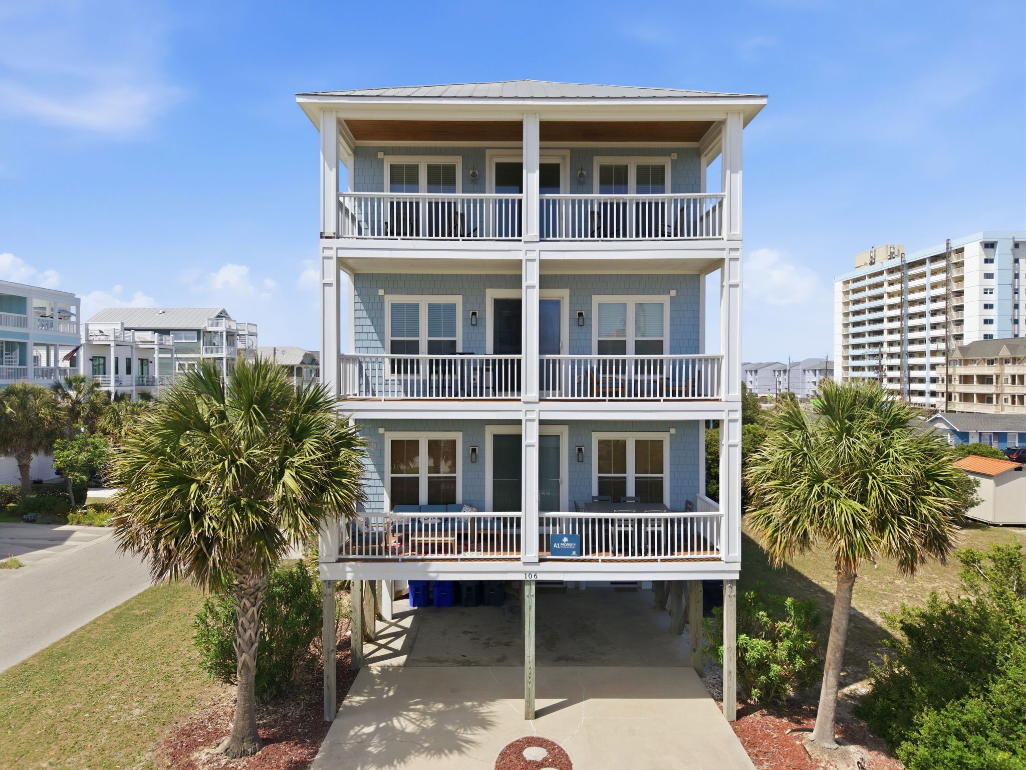 A multi-story building with a balcony on each floor, surrounded by palm trees.