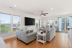 Ein geräumiges Wohnzimmer mit einem großen Flachbildfernseher, zwei grauen Sofas, einem Couchtisch und einem Deckenventilator.