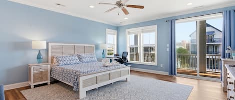 Un dormitorio con cama, mesitas de noche, escritorio, silla, ventilador de techo y vistas al exterior.