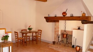 A rustic dining area with a wooden table and chairs, a potted plant, and a brick fireplace with hanging pots. - Rustic Holiday Home in Corciano With Swimming Pool (Corciano)