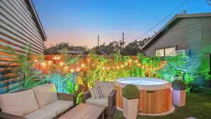 A backyard with a hot tub, outdoor furniture, and string lights.
