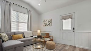 A living room with a grey sectional sofa, a round coffee table, a small rug, and a door with a window.