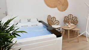 A spa room with a hot tub, two wicker chairs, and a bottle of champagne.