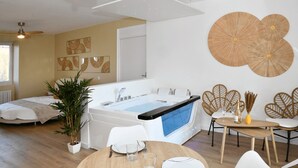 A modern bedroom with a large bed, a sitting area with a table and chairs, a bathtub, and a large mirror.