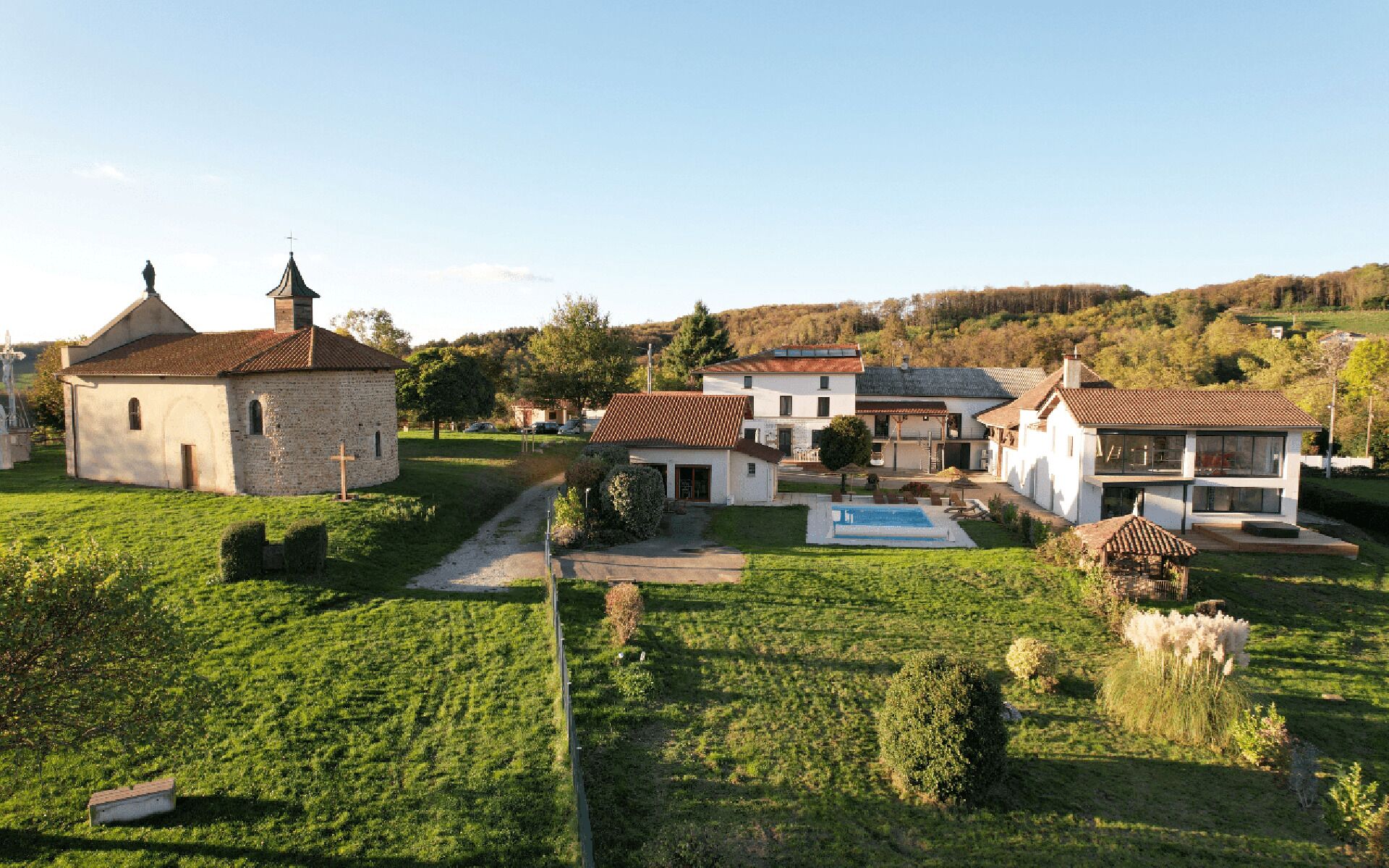 A rural setting with a church, a swimming pool, and a large house with a garden.