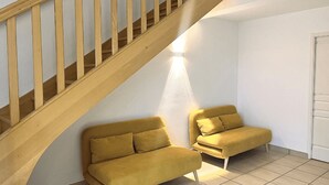Eine Treppe mit hölzernen Geländern führt zu einer Zwischenebene. Auf der Zwischenebene stehen zwei gelbe Sofas.