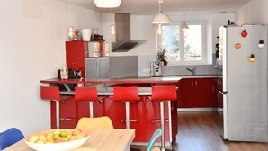 A modern kitchen with red cabinetry, a central island with bar stools, a white refrigerator, and pendant lighting. - Welcome to the" Domaine des étoiles"<br>Enjoy a moment of escape and fun! (GILLONNAY)