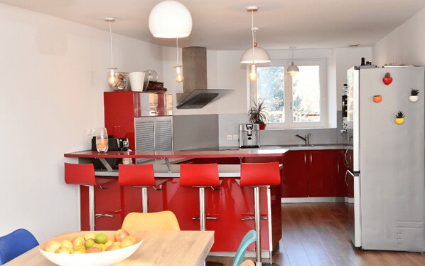 A modern kitchen with red cabinetry, a central island with bar stools, a white refrigerator, and pendant lighting.