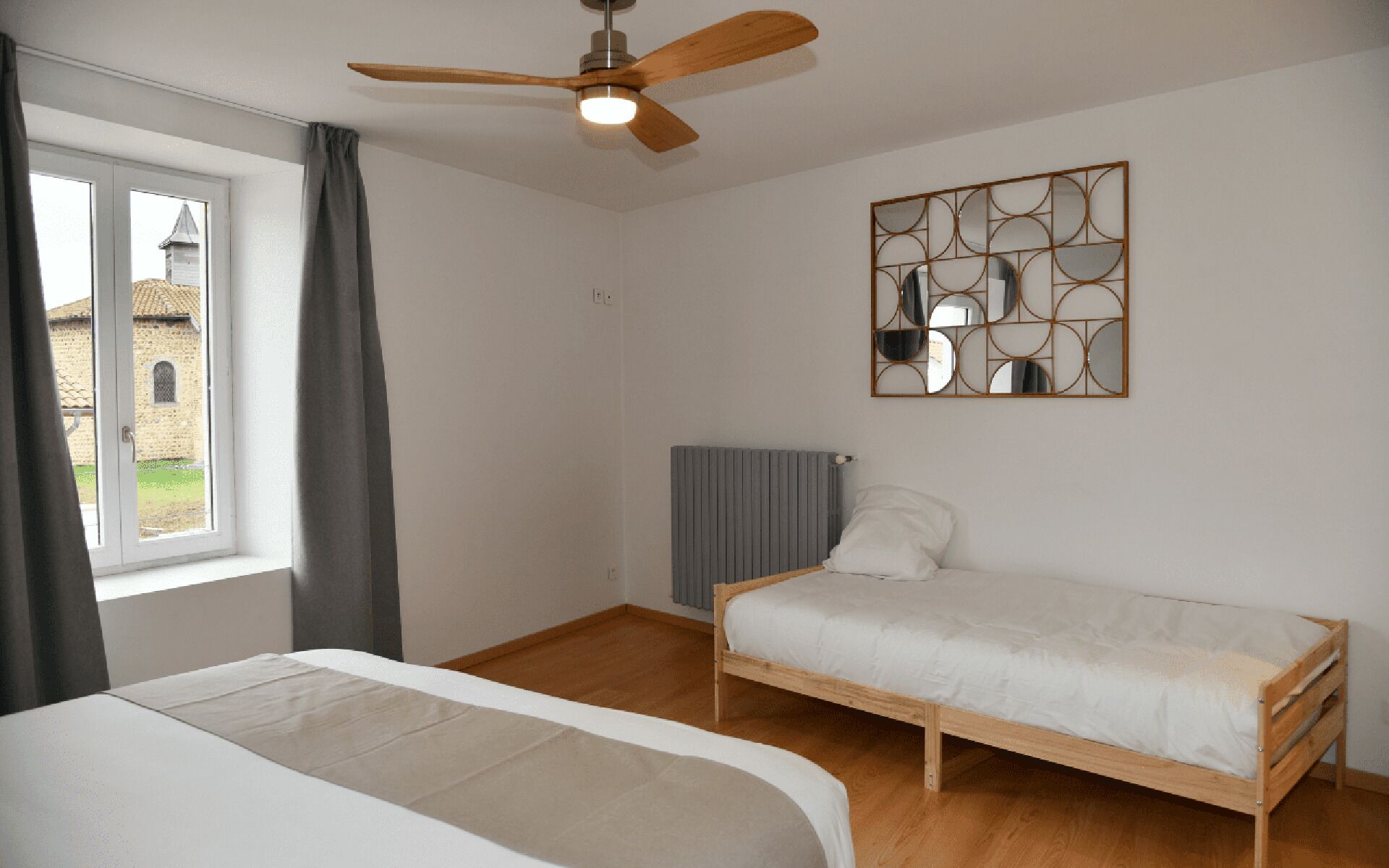 Een slaapkamer met een bed, een plafondventilator, een radiator en een raam met gordijnen.