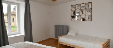 Een slaapkamer met een bed, een plafondventilator, een radiator en een raam met gordijnen.