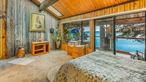 Une chambre avec un grand lit, des murs en bois, un plafond en bois, une fenêtre donnant sur la mer et une petite commode en bois.