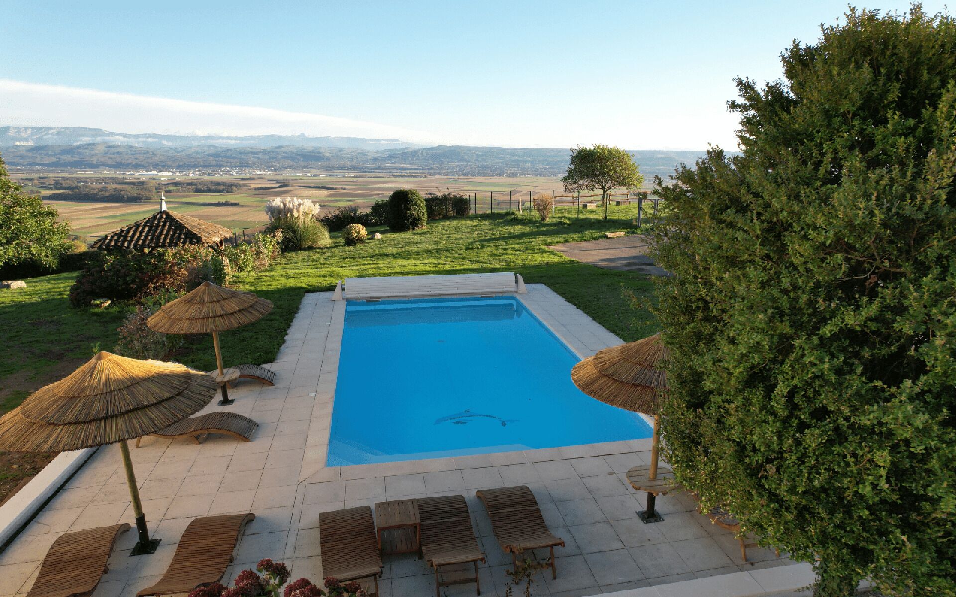 Ein Swimmingpool mit Blick auf die entfernten Hügel, umgeben von Liegestühlen und Sonnenschirmen.