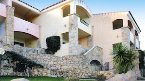 Un immeuble à plusieurs étages, doté d’une façade en pierre et en stuc, de balcons et d’un parterre aménagé avec des rochers et des plantes.
