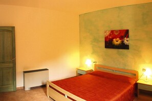 Quarto com cama, duas mesas de cabeceira com luminárias, radiador e porta.