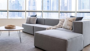 A modern living room with a grey sectional sofa, a round coffee table, and a view of a cityscape through large windows. - Dubai Marina - Stunning Huge 4 Bedroom Apts Near JBR - Gym - Pool - Parking (Dubai)