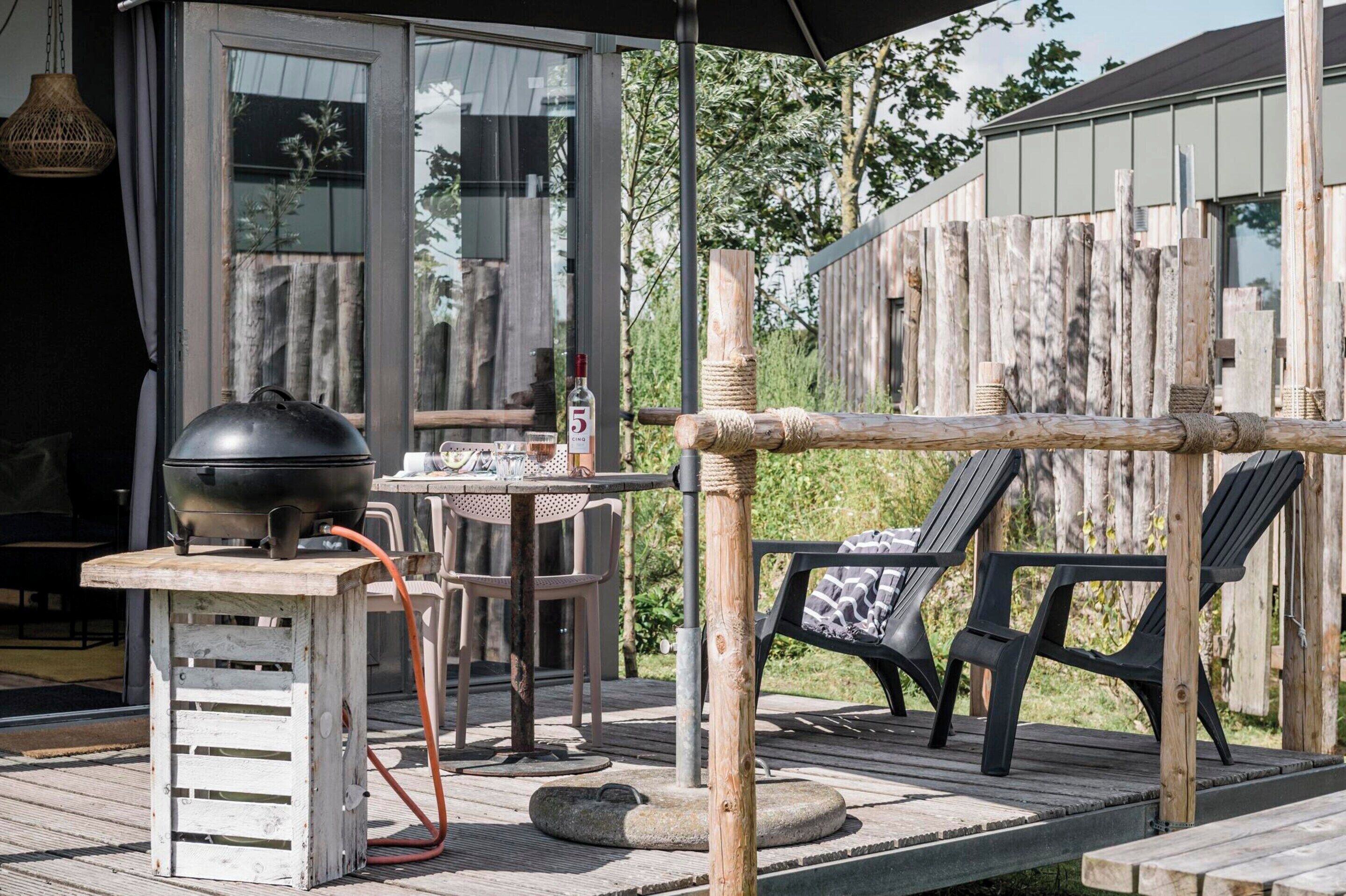 Eine Terrass mit Grill, Tisch, Stühlen und Holzlattenzaun.