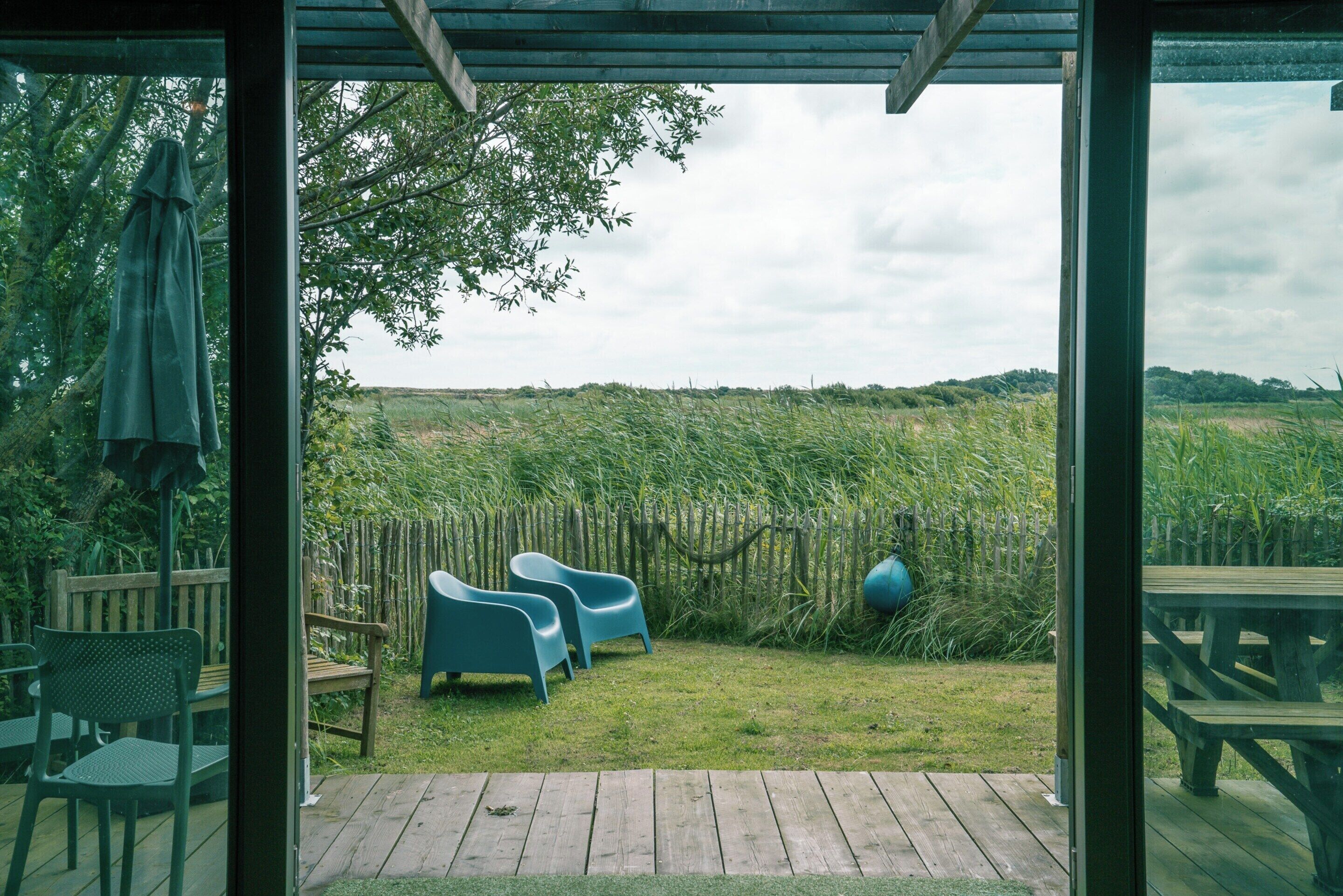Une terrasse extérieure avec un plancher en bois, un banc en bois et deux chaises bleues.