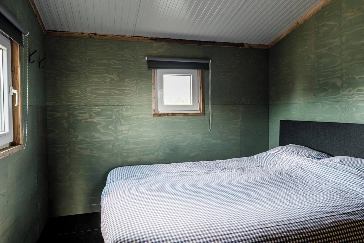 A bedroom with a bed, a window with a blind, and green walls.