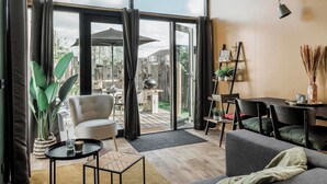 A modern living room with a sofa, a dining table, and a large sliding glass door leading to an outdoor patio. - Apartment With Terrace With Sufficient Garden (Callantsoog)