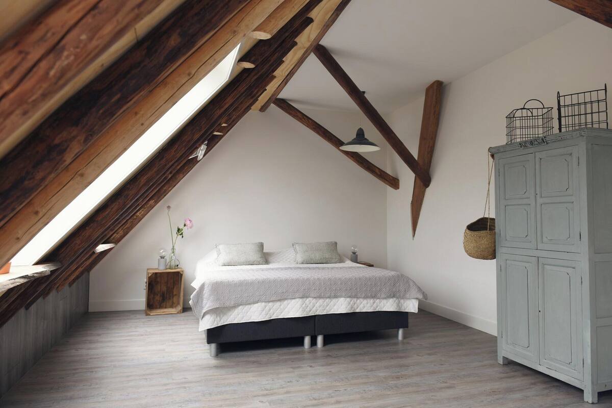 A bedroom with a sloped ceiling, a bed, a wooden cabinet, and a hanging basket.